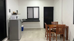 A compact kitchen with a refrigerator, microwave, and a small window. There is a dining table with chairs and a black door. - Studio on Cancun Downtown. Close to grocery stores, restaurants and bus stop. (Cancún)