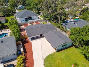 Houses with diverse roof styles surround a well-manicured lawn and a swimming pool, set amidst a lush tree-lined environment.