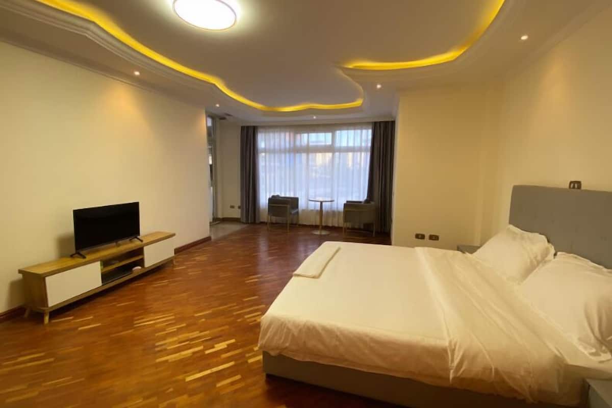 Ein Hotelzimmer mit einem großen Bett, einem Fernseher auf einem Holzboden, einem kleinen Tisch und einem Stuhl.