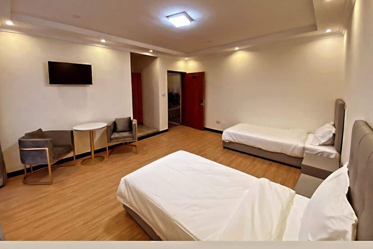 Ein Hotelzimmer mit zwei Betten, einem Fernseher, einem kleinen Tisch und einem Sofa.