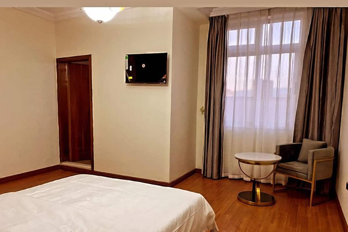 Ein Hotelzimmer mit einem großen Bett, einem kleinen runden Tisch, einem Sessel, einer Tür und einem Fenster mit Vorhängen.