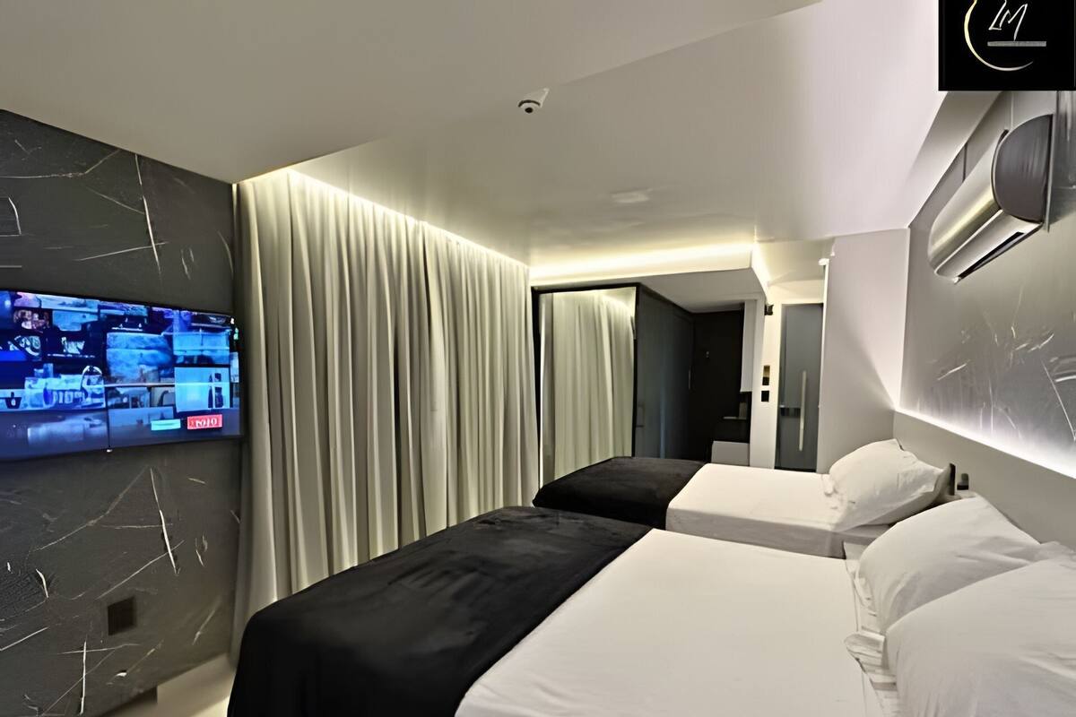 A modern hotel room with two beds, a flat-screen TV mounted on the wall, and a large window with curtains.