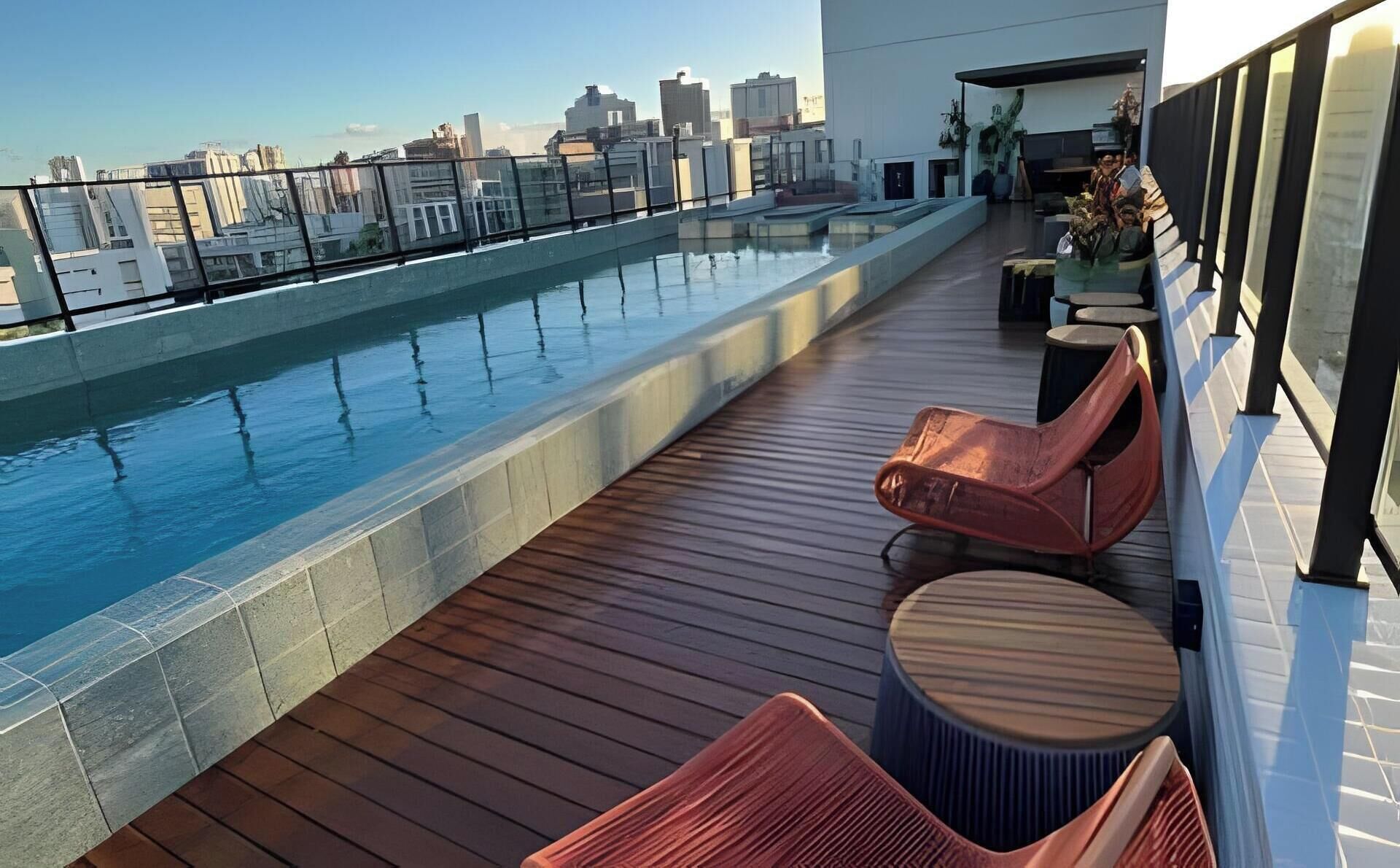 A rooftop pool with a city view, wooden deck, and seating areas.