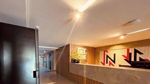A modern reception area with a reception desk, a wall-mounted sign, and a hallway leading to other rooms. - LM HOSPEDAGENS - GET ONE (João Pessoa)