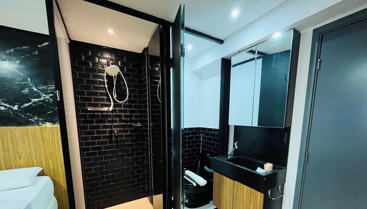 Une salle de bain moderne avec une douche carrelée de noir, des toilettes blanches et un meuble-lavabo en bois avec un miroir.
