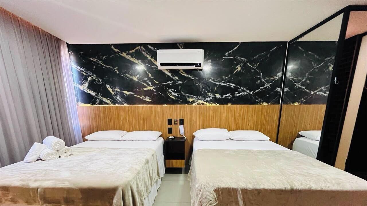 Habitación de hotel con dos camas, cabecera de madera, pared con estampado de mármol, unidad de aire acondicionado y teléfono.