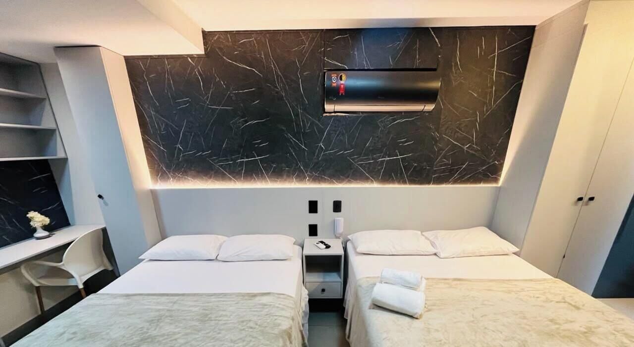 Habitación de hotel con dos camas, un escritorio y aire acondicionado integrado.