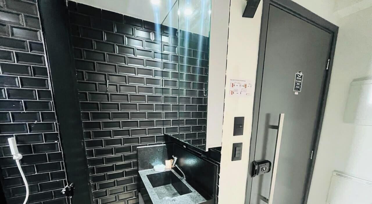 Ein Zimmer mit schwarzer Backsteinwand, einem kleinen Waschbecken und einer Tür mit Griff.