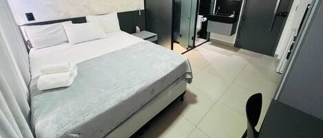 A hotel room with a bed, bedside table, and a small desk with a chair.