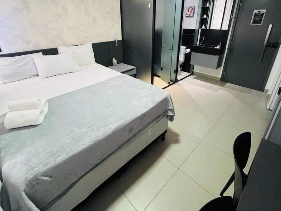 A hotel room with a bed, bedside table, and a small desk with a chair.