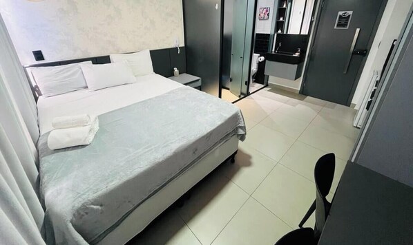 A hotel room with a bed, bedside table, and a small desk with a chair. - LM HOSPEDAGENS - GET ONE (João Pessoa)