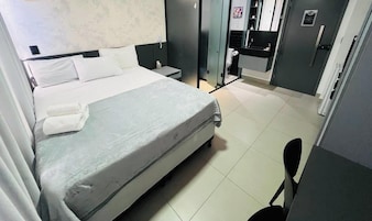 Quarto de hotel com cama, mesa de cabeceira e pequena escrivaninha com cadeira.