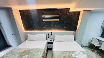 A hotel room with two beds, a desk, a chair, an air conditioning unit, and a minibar.