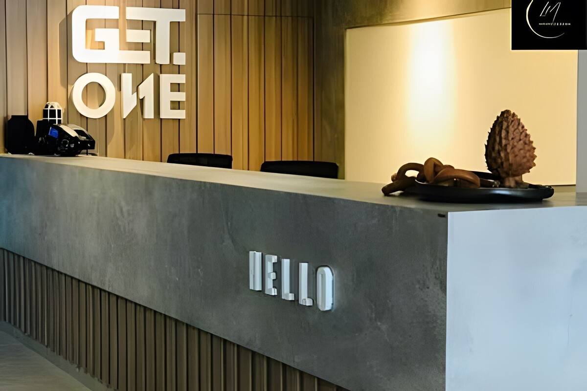 A reception desk with a 'HELLO' sign, a wooden panel wall, and a 'GET. ONE' sign.