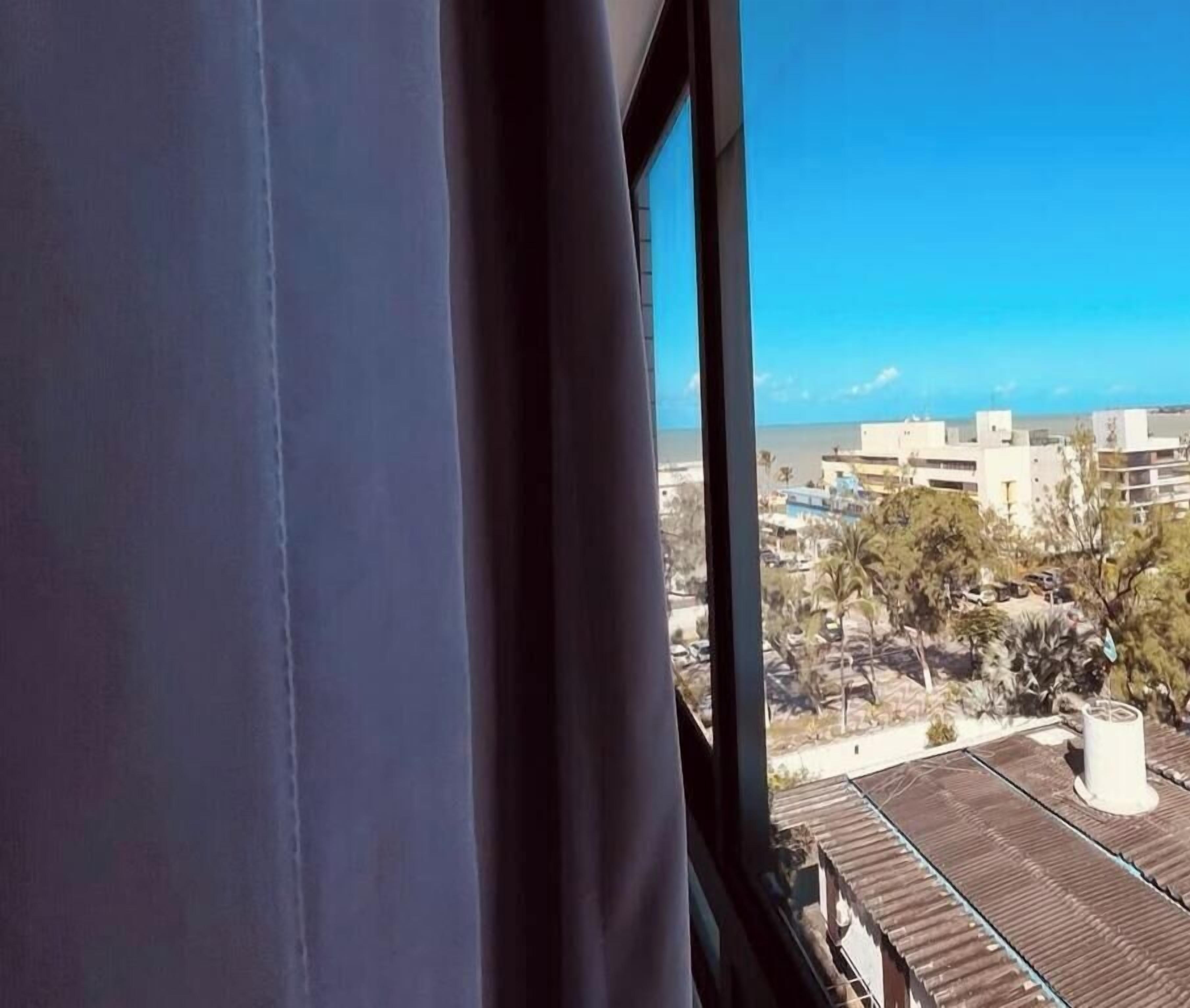 A view through a window with a curtain, overlooking a residential area with houses and trees.