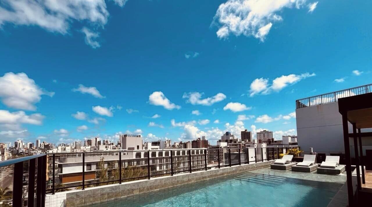 A rooftop pool with lounge chairs, a city skyline in the background, and a clear sky.
