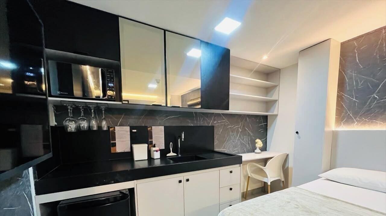A modern kitchen with a black countertop, white cabinets, and a built-in microwave. There is a small seating area with a chair and a table.
