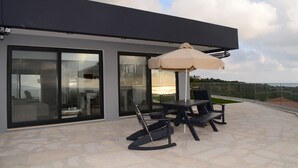 Un patio exterior moderno con una mesa, sillas, un paraguas grande y vistas al paisaje.