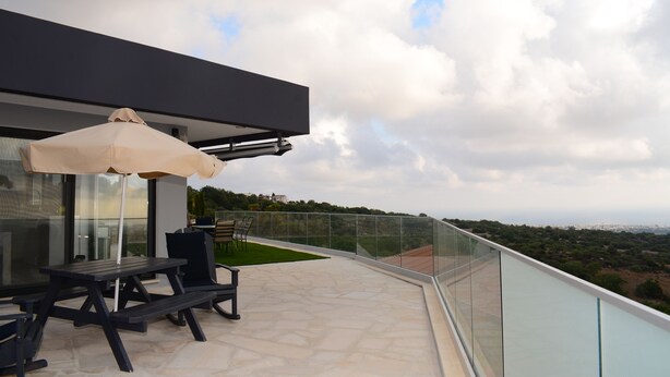 Un patio moderno al aire libre con balaustrada de vidrio, una mesa de picnic y una sombrilla.