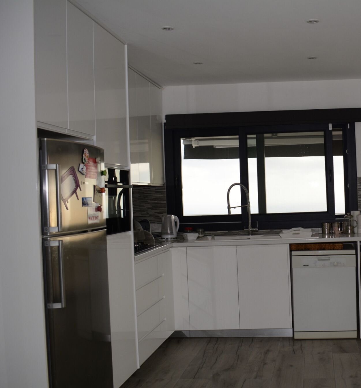 A modern kitchen with white cabinetry, a stainless steel refrigerator, a built-in oven, a coffee maker, and a dishwasher.