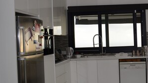 Cocina moderna con armarios blancos, refrigerador de acero inoxidable, horno empotrado, cafetera y lavavajillas.