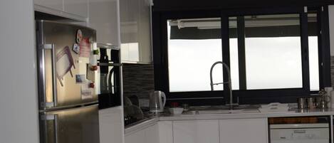 A modern kitchen with white cabinetry, a stainless steel refrigerator, a built-in oven, a coffee maker, and a dishwasher.