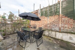 A patio with a glass table and six chairs, an umbrella, and a brick wall. - Spacious 4BR London Home Near Train, ExCeL & O2 (London)