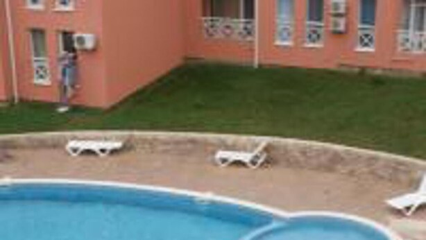 A swimming pool with a small hot tub, surrounded by lounge chairs and people relaxing on towels. - Beautiful 1-bed Studio in Sunny Beach Bulgaria (Nessebar)
