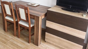 A wooden dining table with four chairs, a television on a cabinet, and a small remote control. - Beautiful 1-bed Studio in Sunny Beach Bulgaria (Nessebar)