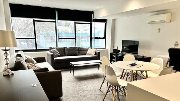 A modern living room with a sofa, a coffee table, a TV, and a dining area with chairs and a table.