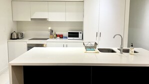 A modern kitchen with white cabinetry, a central island, a microwave, and a sink.
