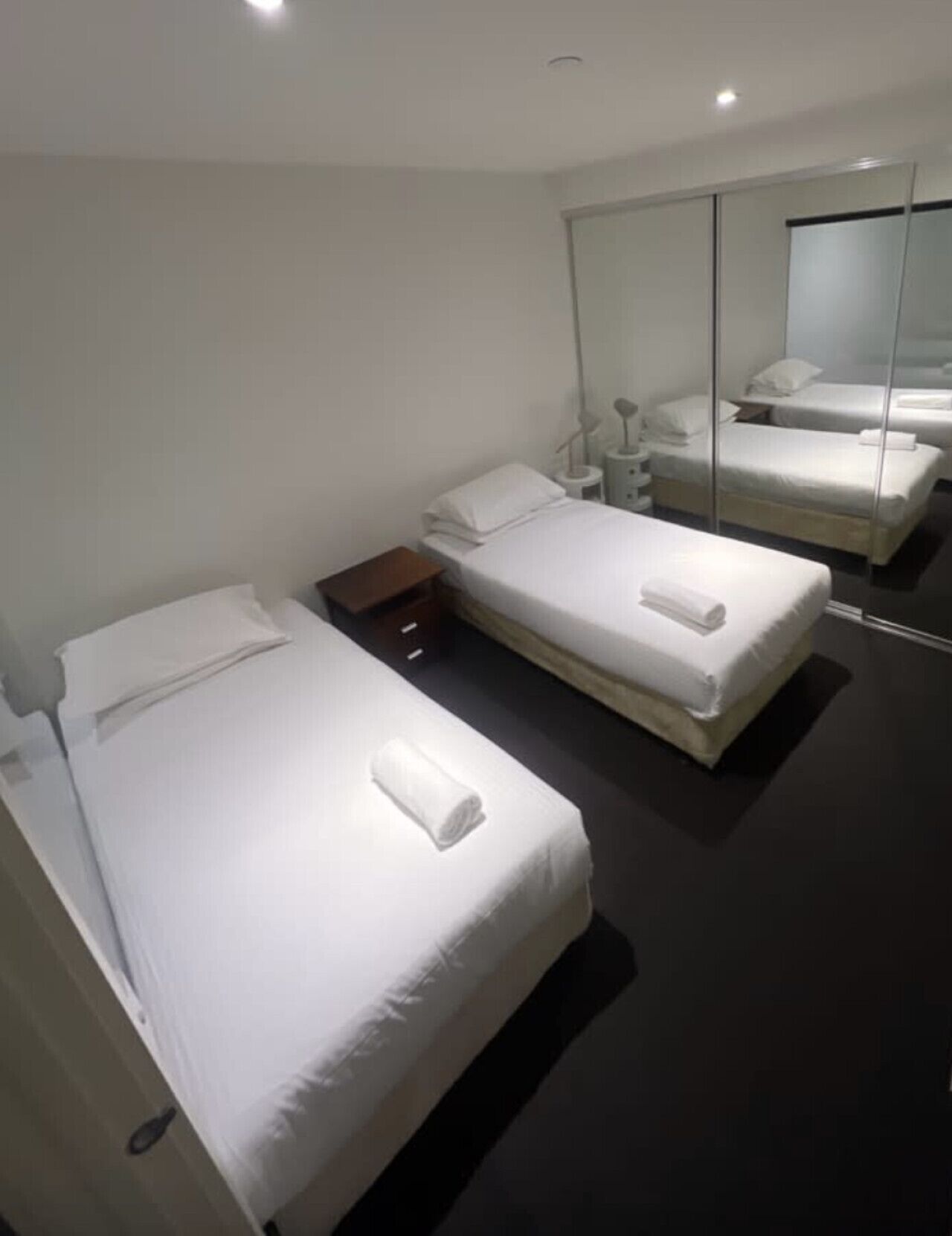 Une chambre d’hôtel moderne avec deux lits simples, une petite table de chevet, une commode et un grand miroir.