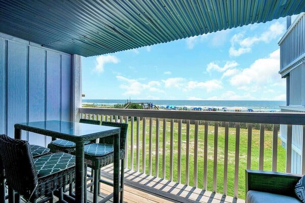 A balcony with a view of the ocean, wicker furniture, and a wooden deck.