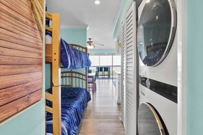 A bunk bed with a blue striped bedspread, a wooden wall panel, and a washing machine.