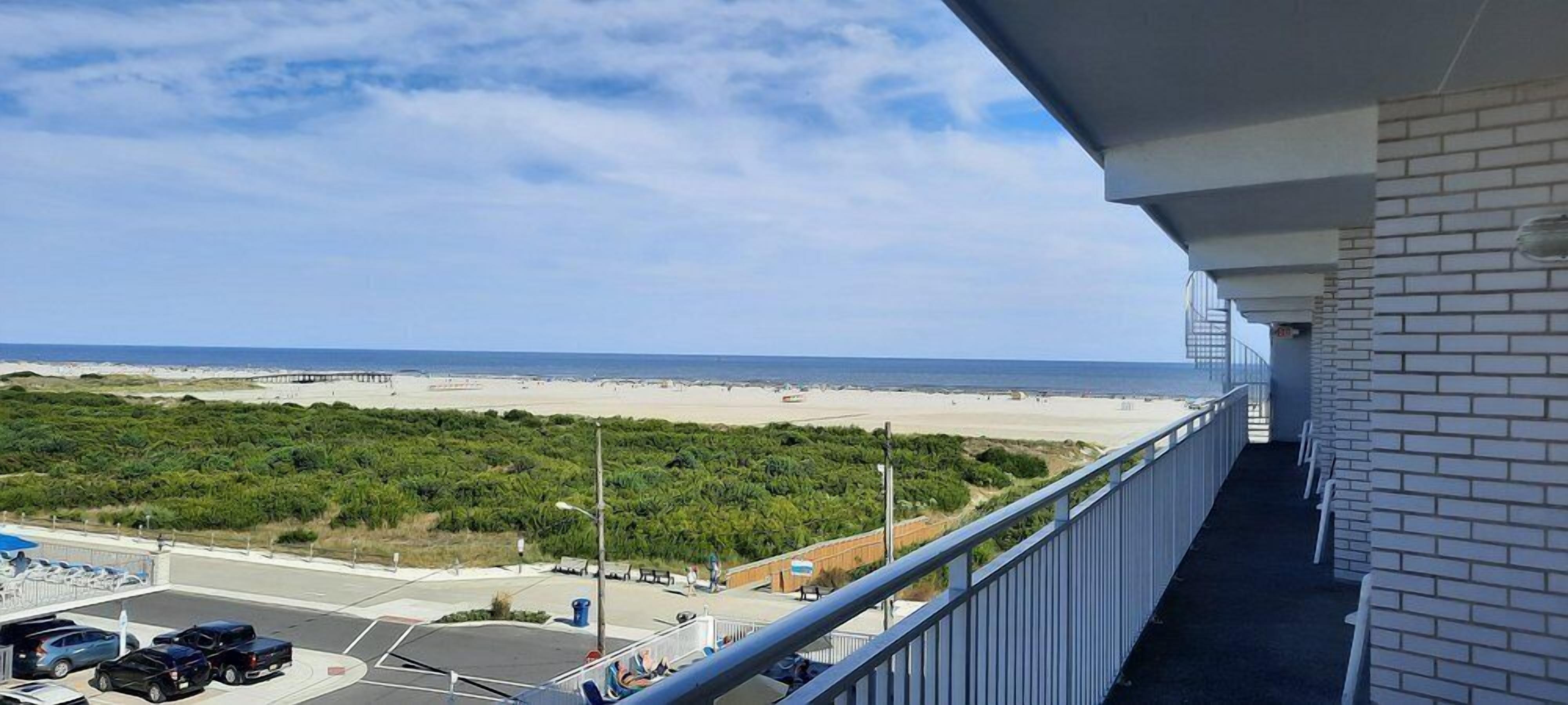 Un balcon avec vue sur la plage, un espace de stationnement et un mur en briques.