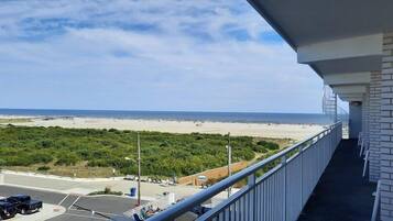 Un balcon avec vue sur la plage, un espace de stationnement et un mur en briques.