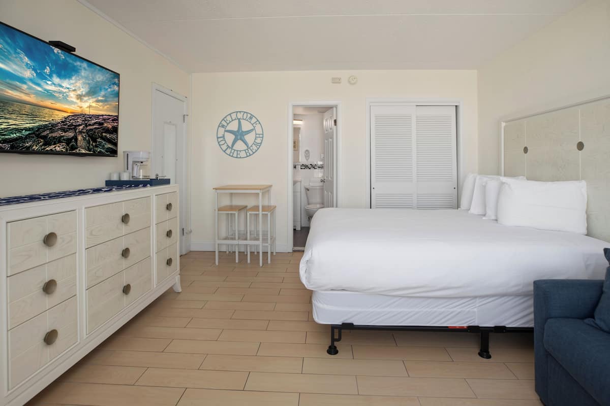Une chambre à coucher comprenant un lit, une commode, une machine à café, une petite table, une chaise et une horloge murale.