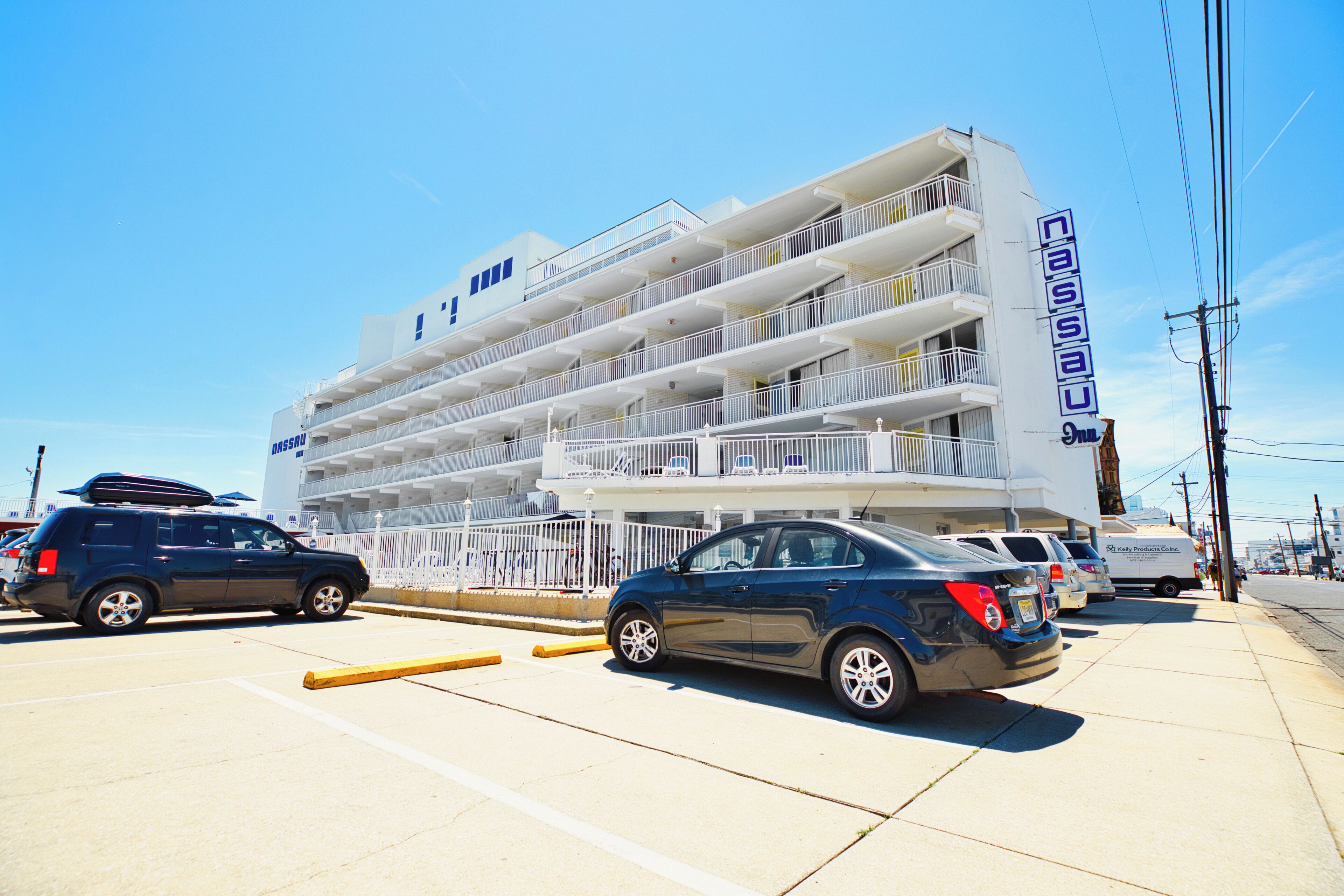 A multi-story hotel with balconies, a parking lot, and a clear blue sky.