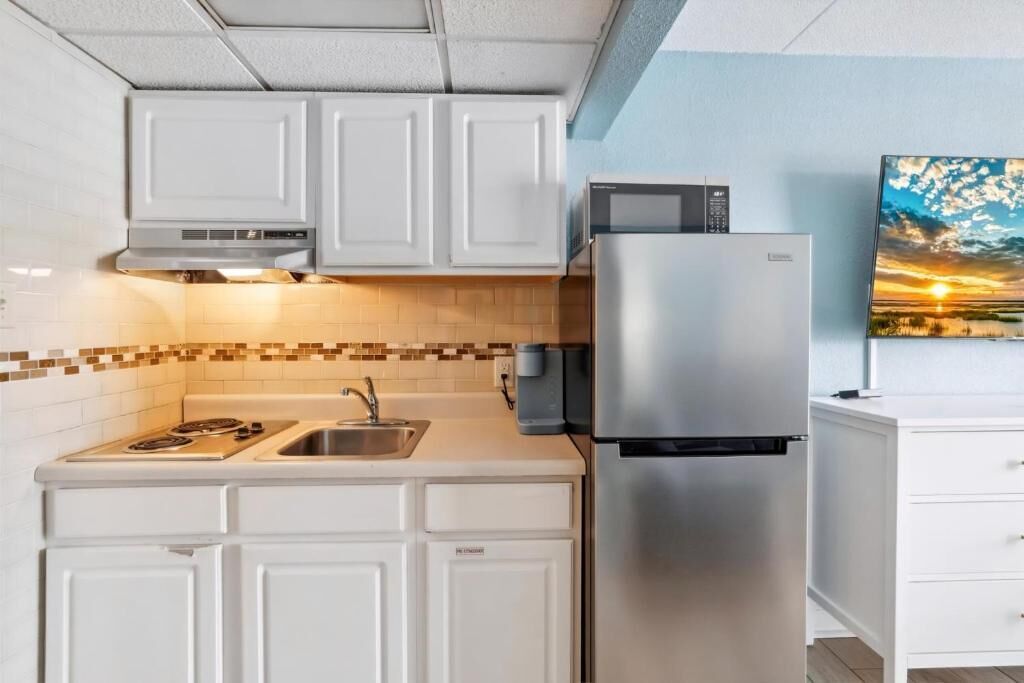 A kitchen with white cabinets, a stainless steel refrigerator, a microwave, and a tiled backsplash.