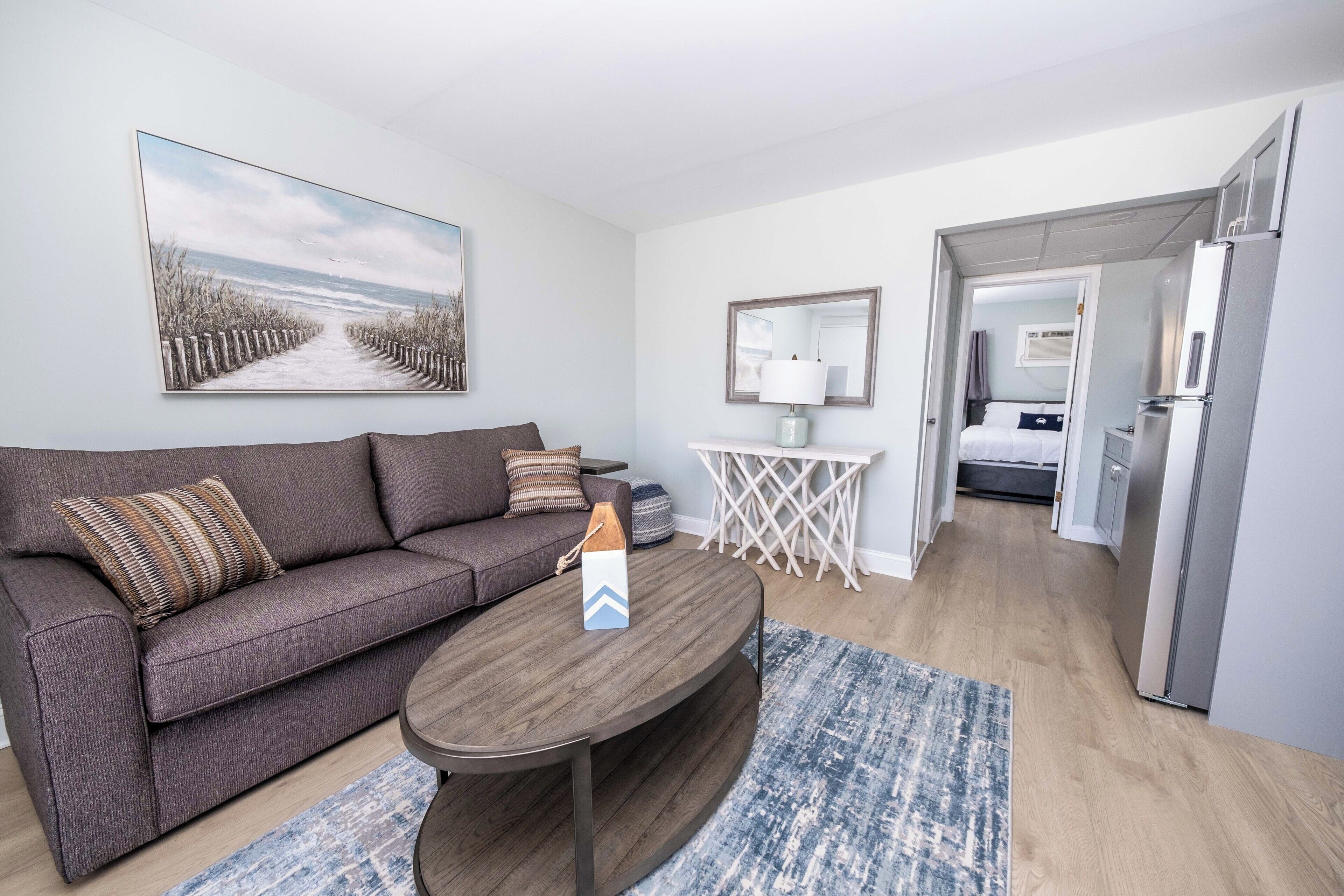 A modern living room with a sofa, coffee table, and a painting of a beach pathway.