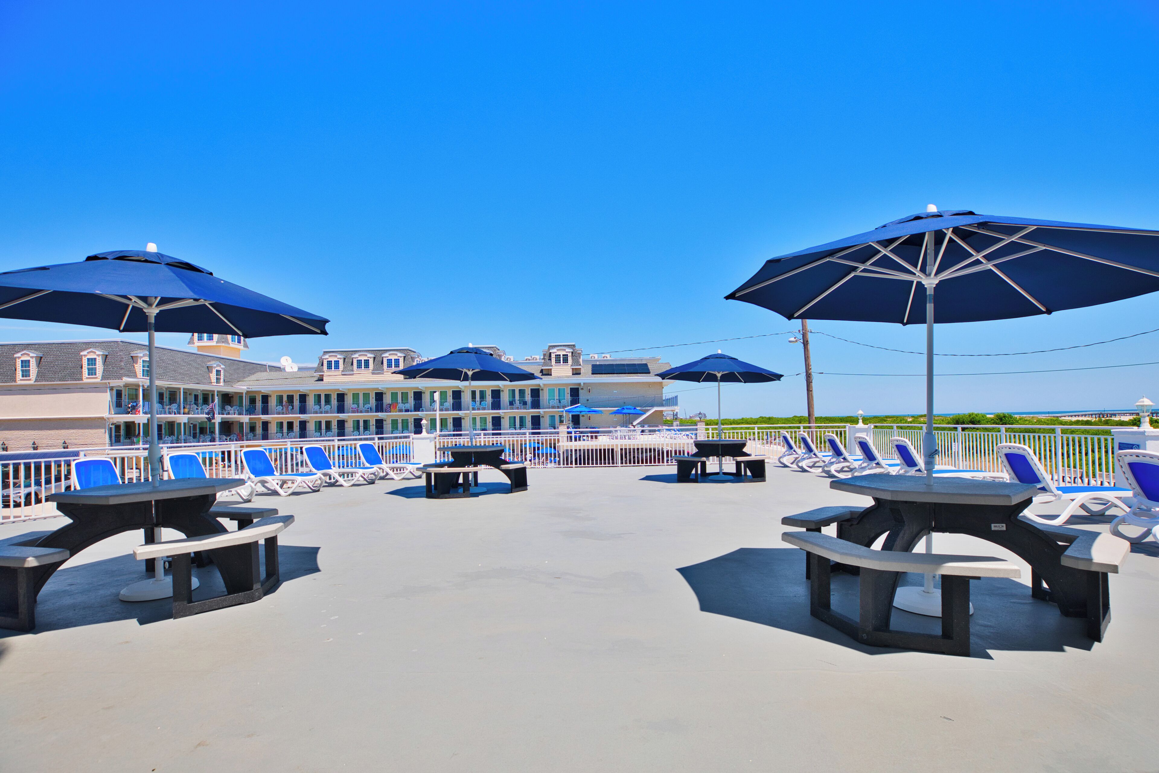 Une terrasse sur le toit avec des chaises longues et des tables de pique-nique, un ciel bleu dégagé et un bâtiment en arrière-plan.