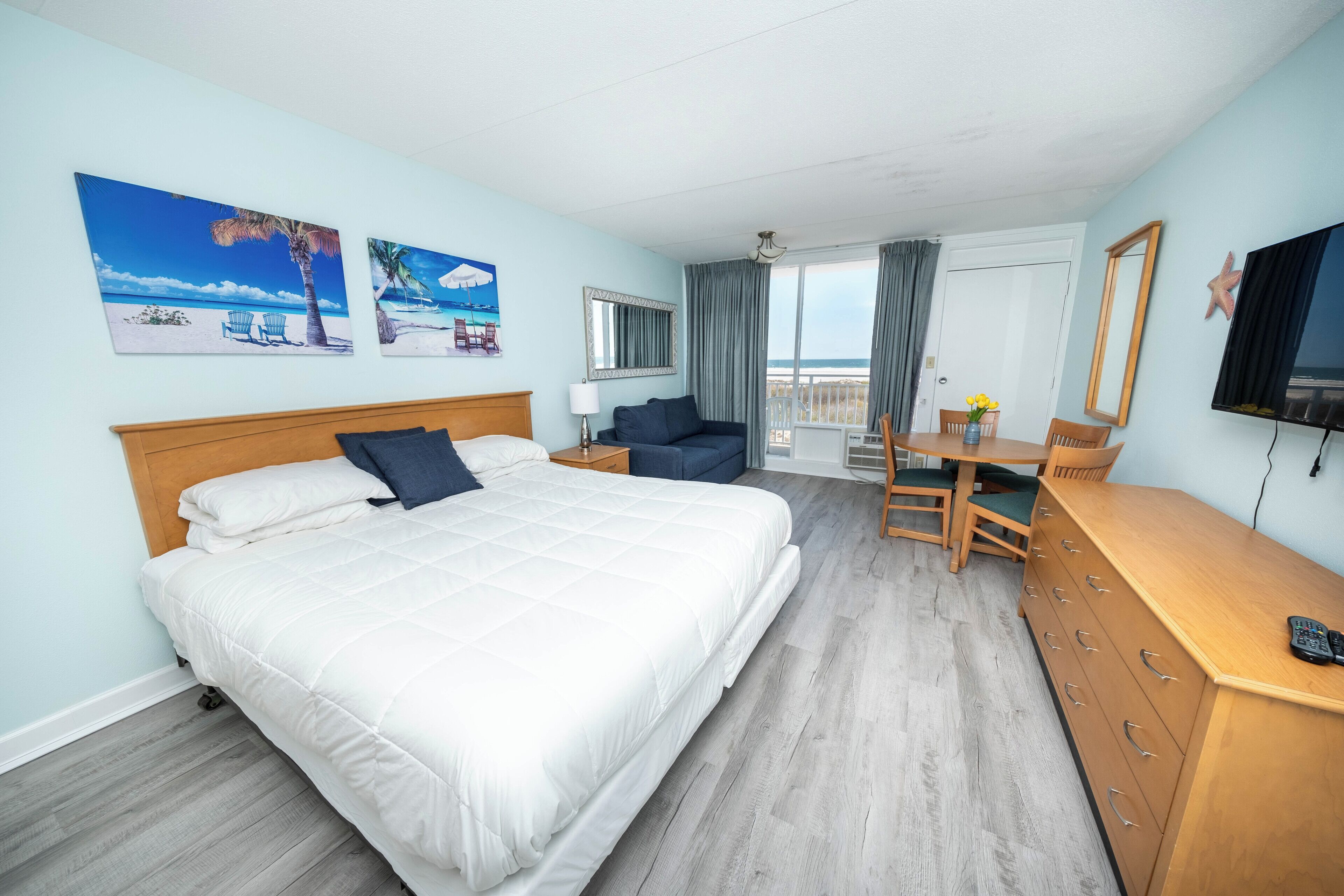 A hotel room with a bed, a desk, a dresser, a TV, and a balcony with a view.