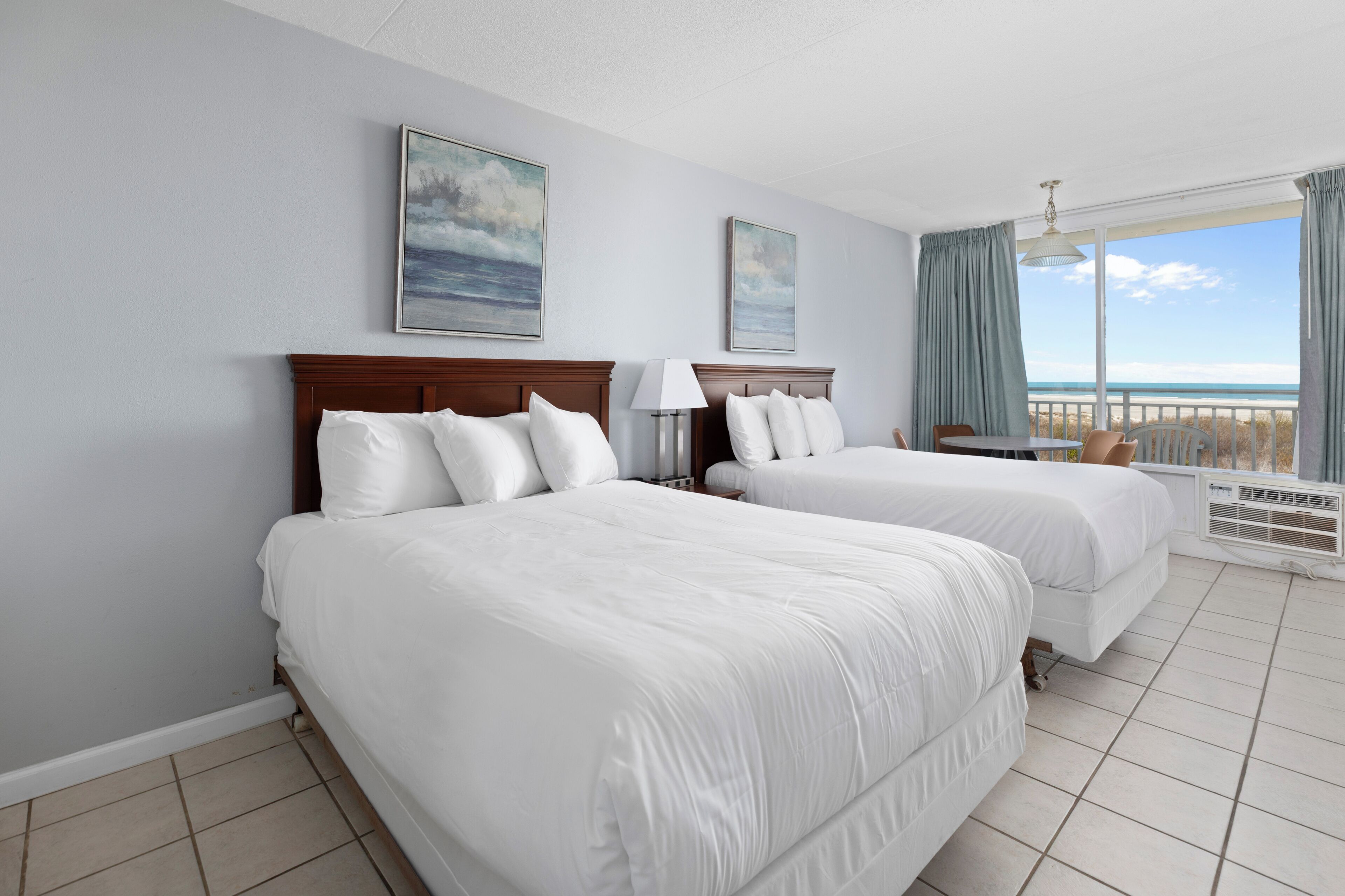 A hotel room with two beds, a balcony with a view of the beach, and a ceiling fan.