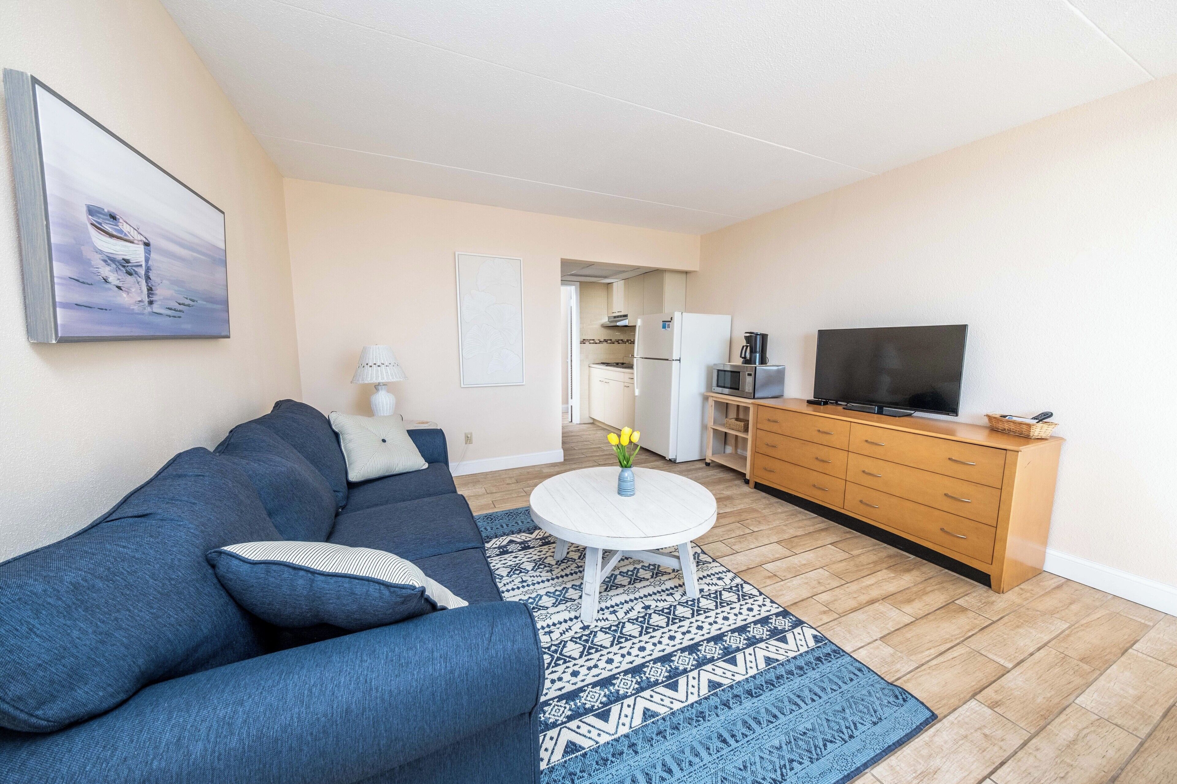 A living room with a sofa, a coffee table, a television, and a kitchen in the background.