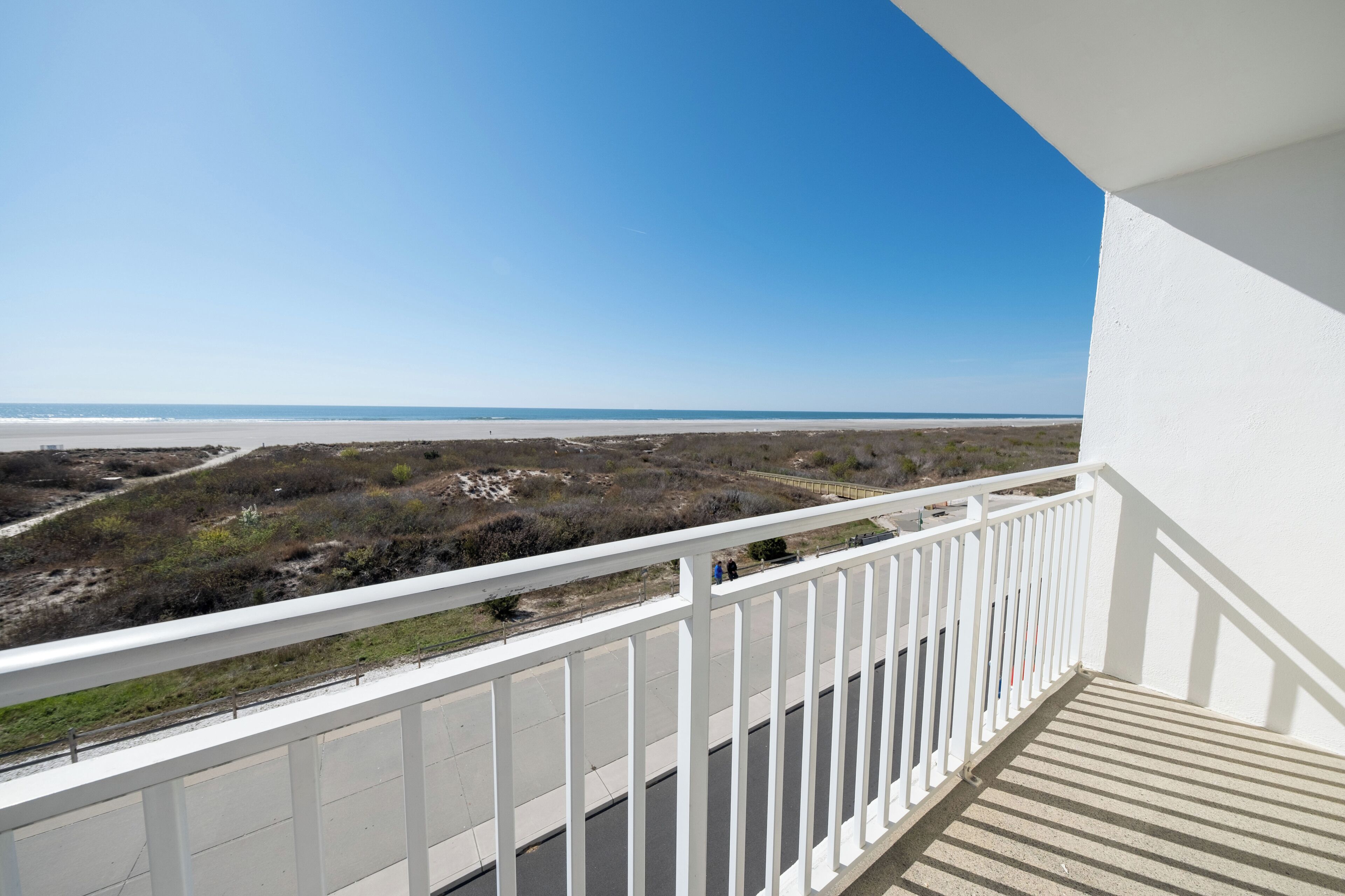 A balcony with a view of the beach and a clear sky.