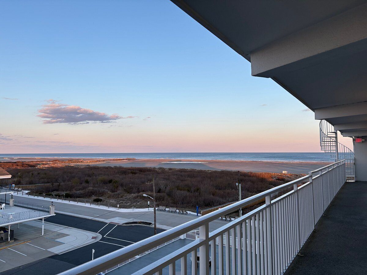 A balcony with a view of a beach and a parking lot.