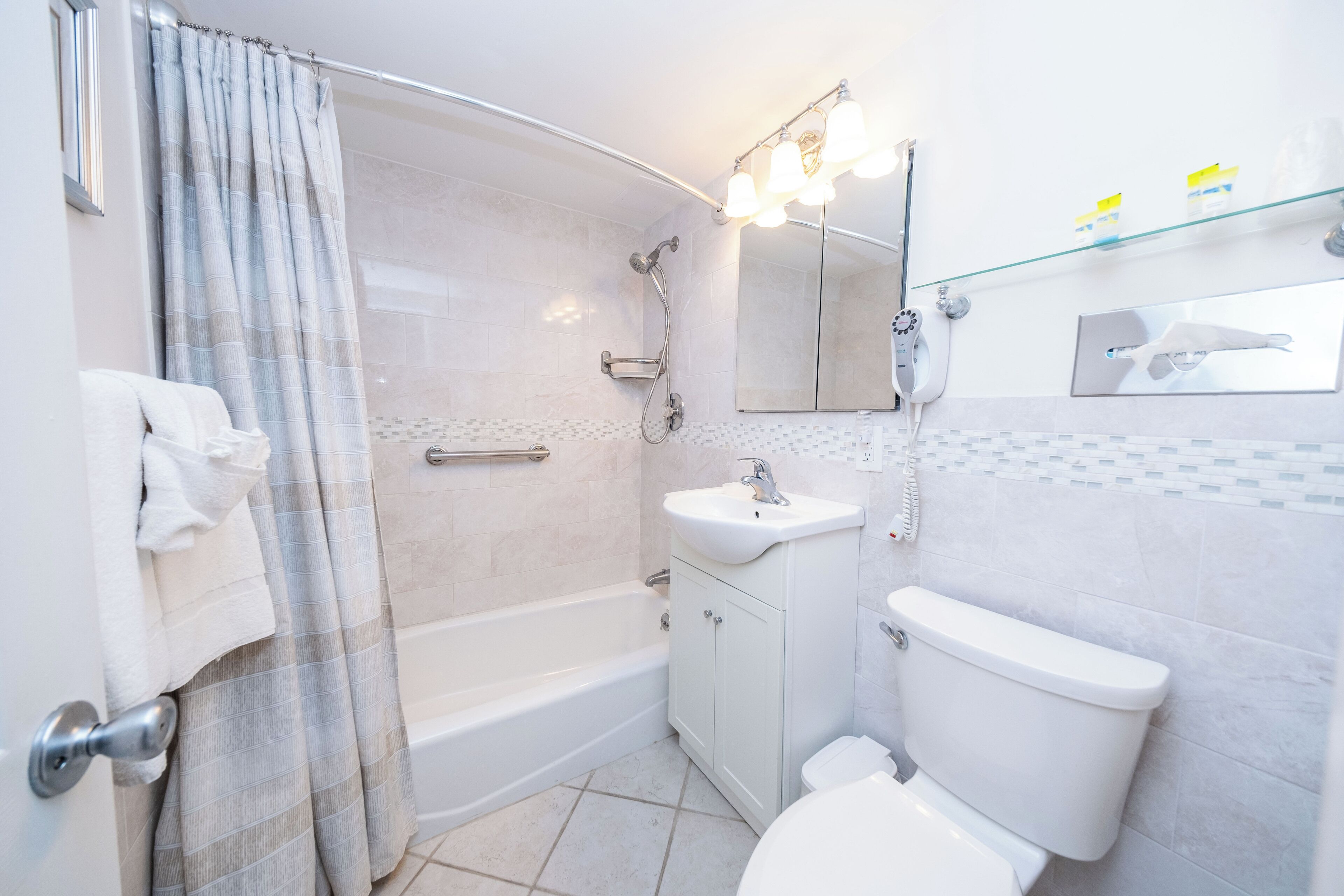 A modern bathroom with a shower, toilet, sink, and a glass shelf with toiletries.