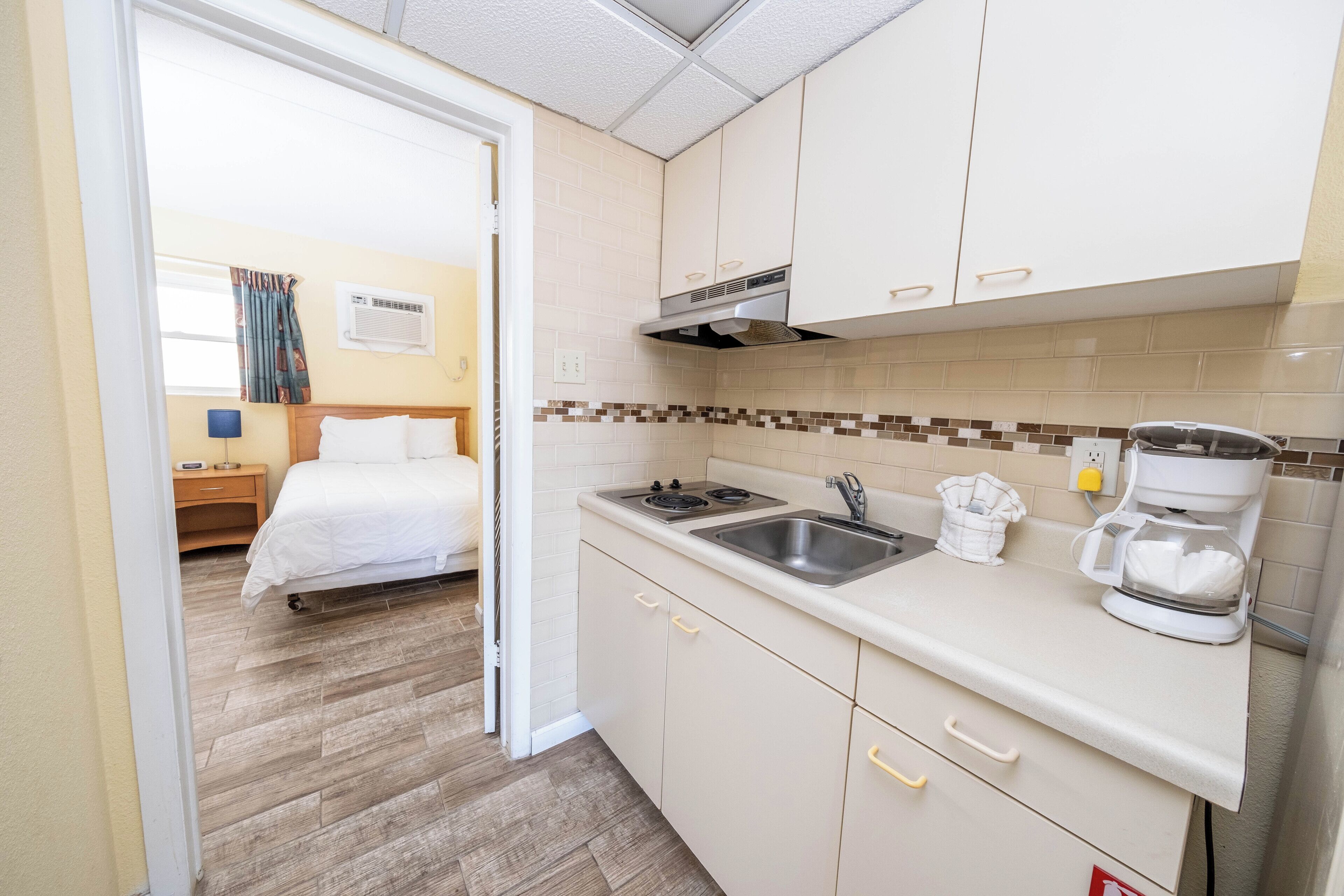 A compact hotel room with a kitchenette, a bed, and a bathroom visible through an open door.