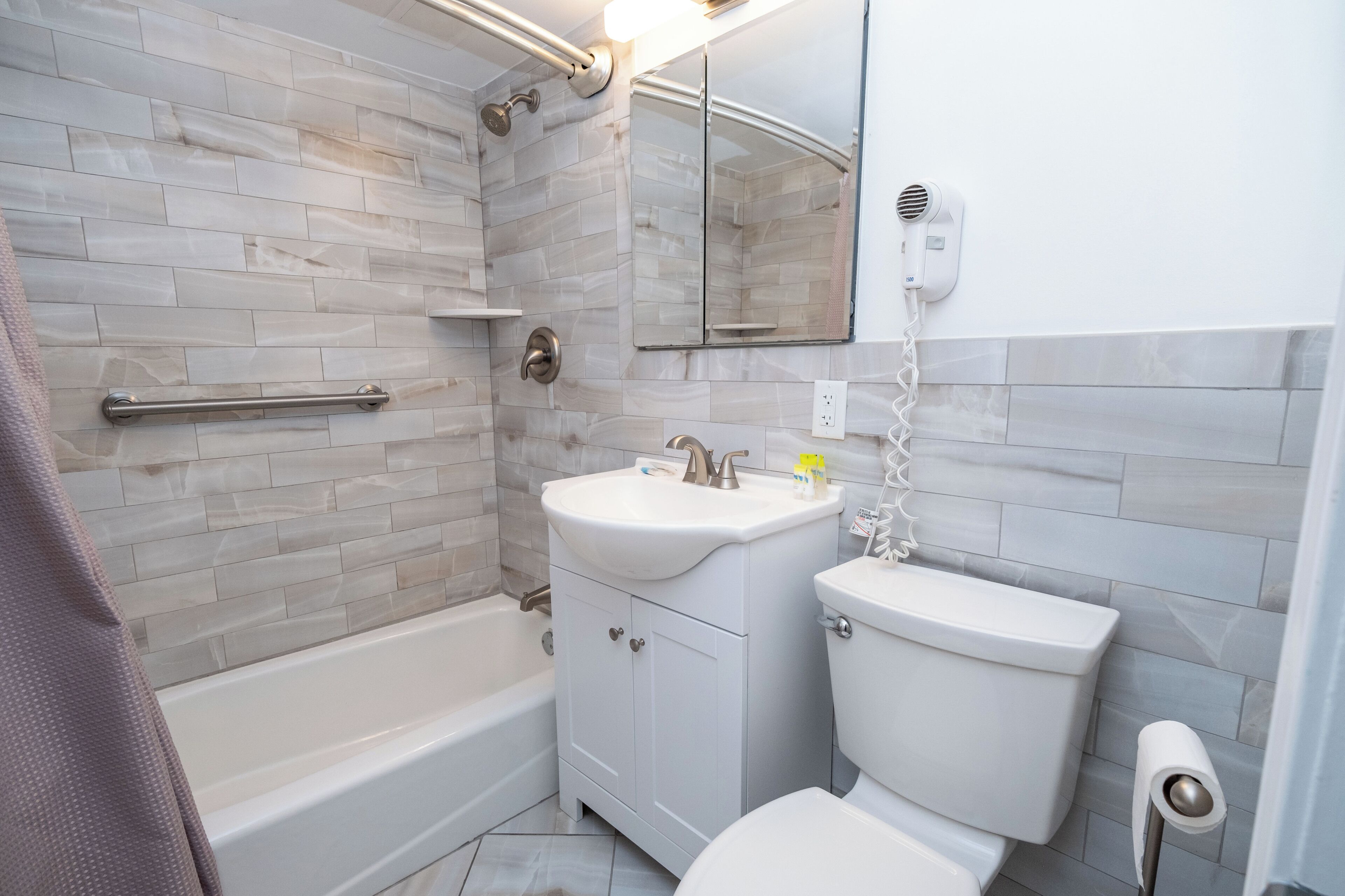 Une salle de bain équipée d’une baignoire, d’un lavabo, de toilettes et d’un sèche-cheveux fixé au mur.