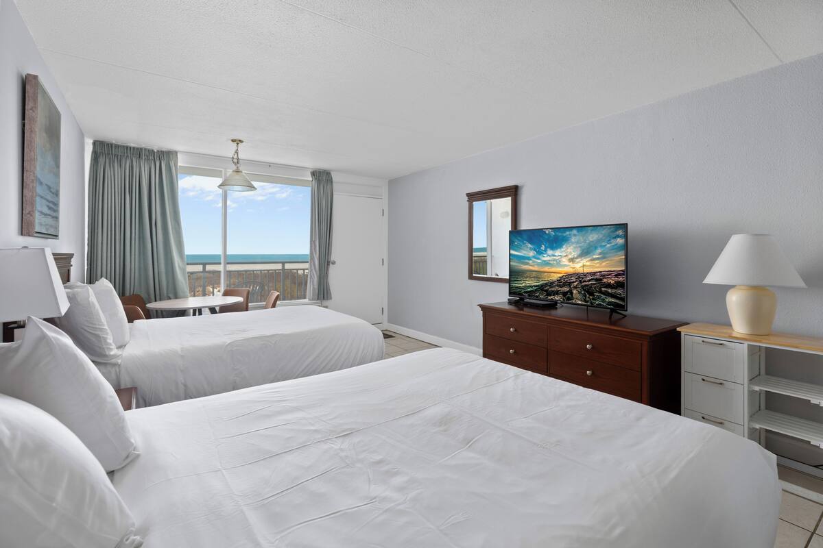 Une chambre d’hôtel avec deux lits, une télévision, un bureau et un balcon avec vue.